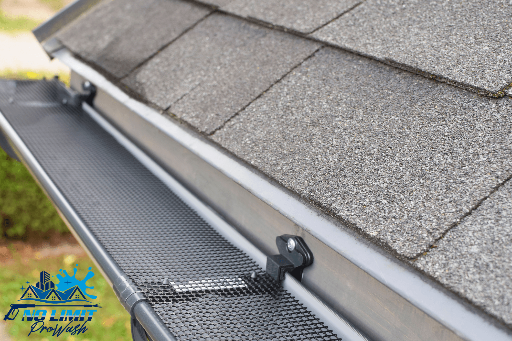 Black mesh gutter guard installed on a metal gutter along a grey shingled roof edge.